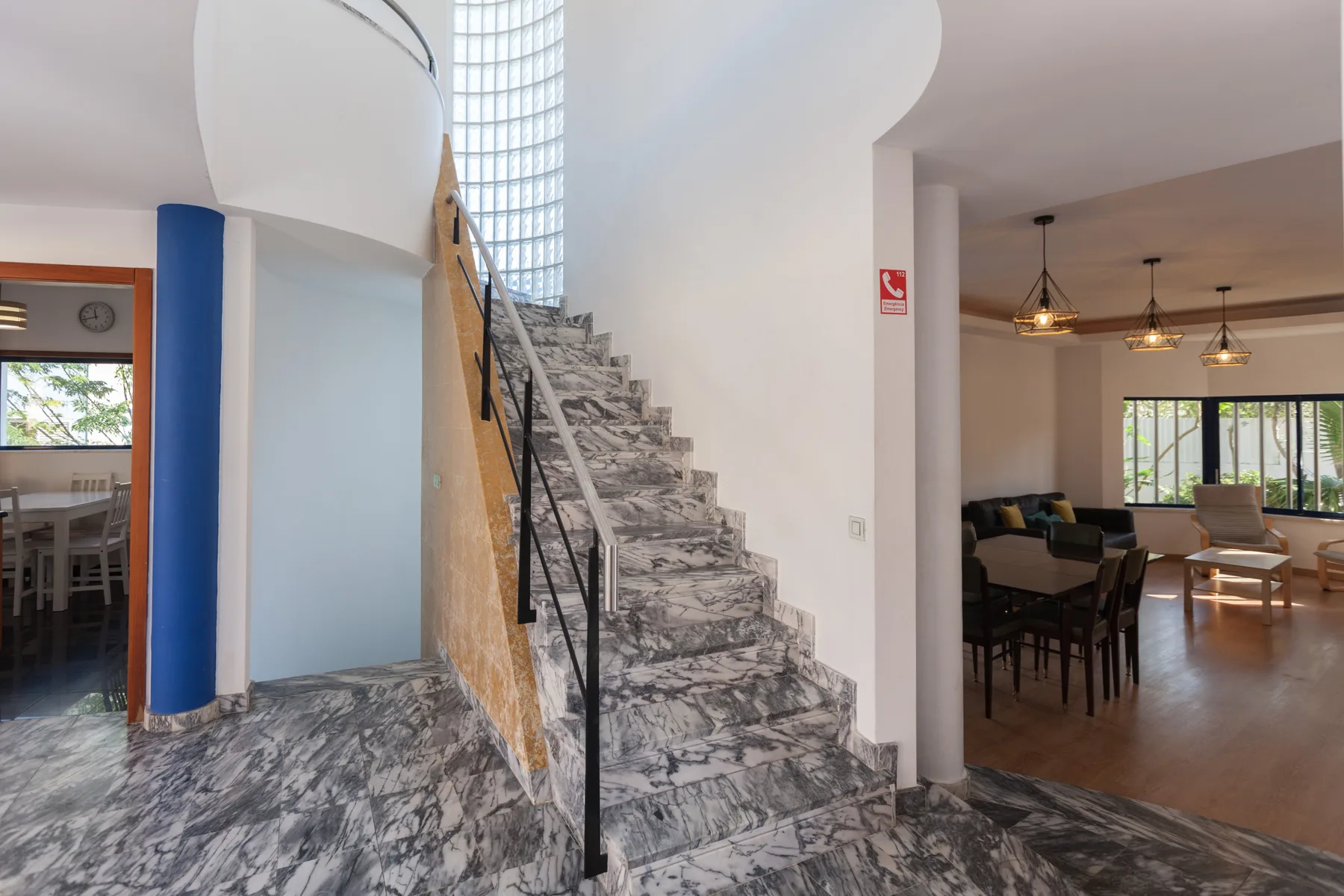 A marble staircase rises between a dining area and a living room.