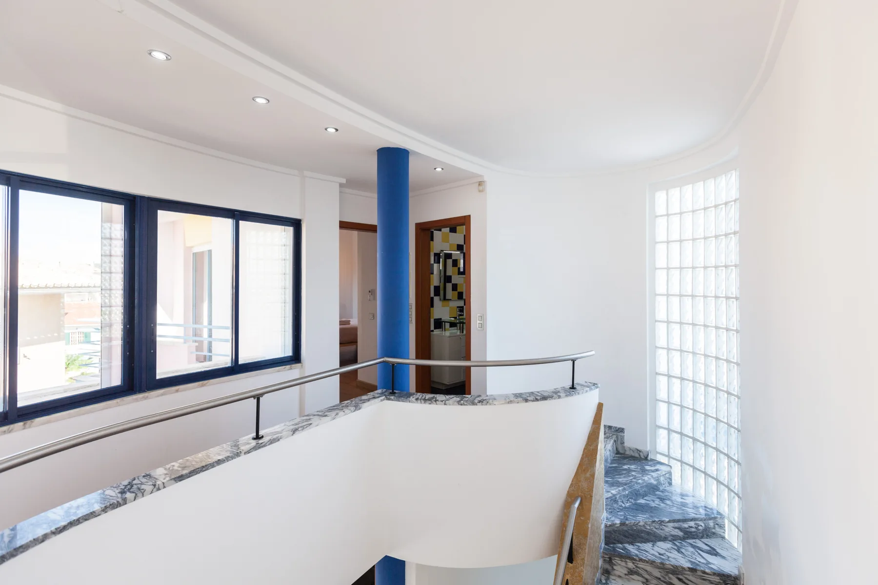 A bright interior landing with large windows and a curved white railing.