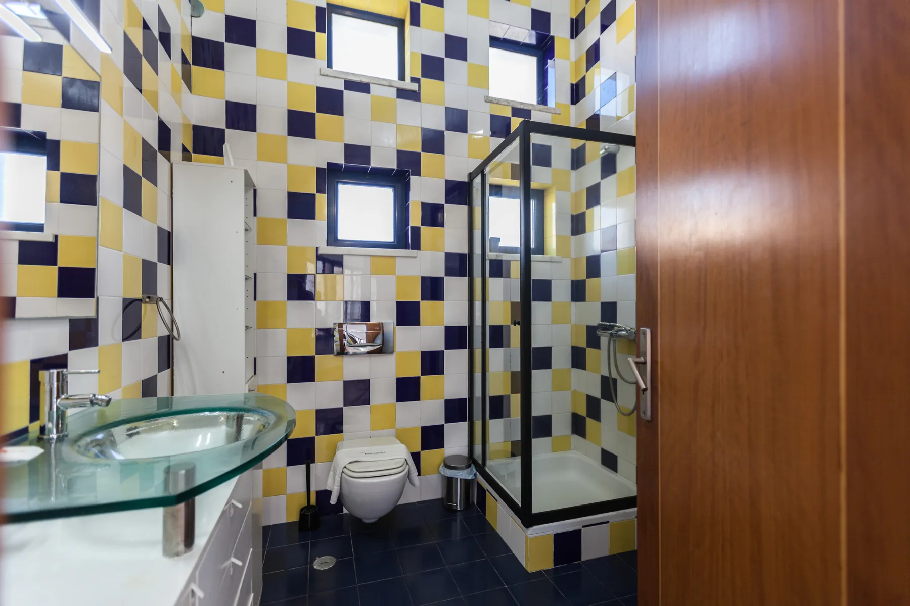 A tiled bathroom with a glass shower and a wall-mounted sink.