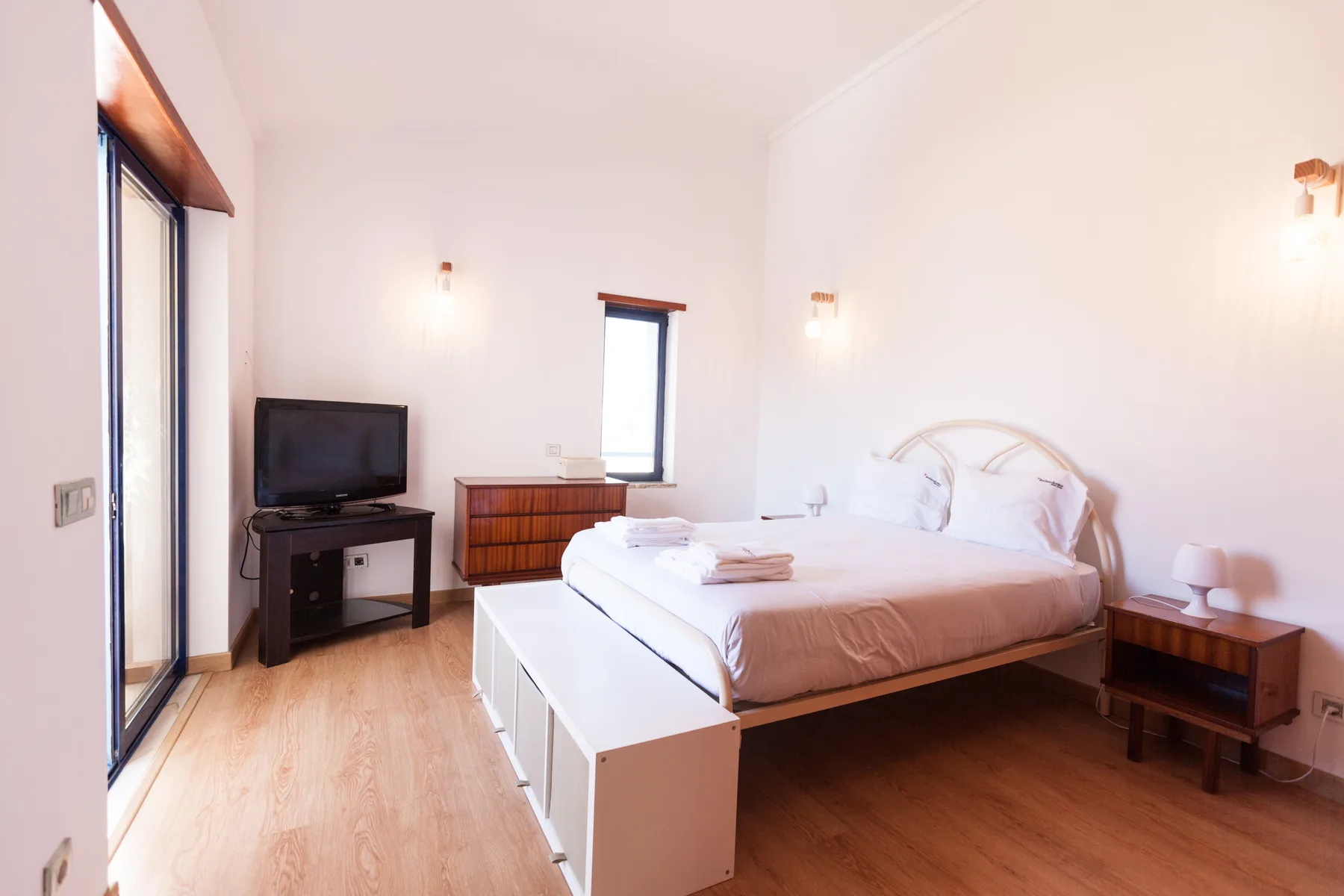 A bright bedroom with a bed, bedside tables, and a television.