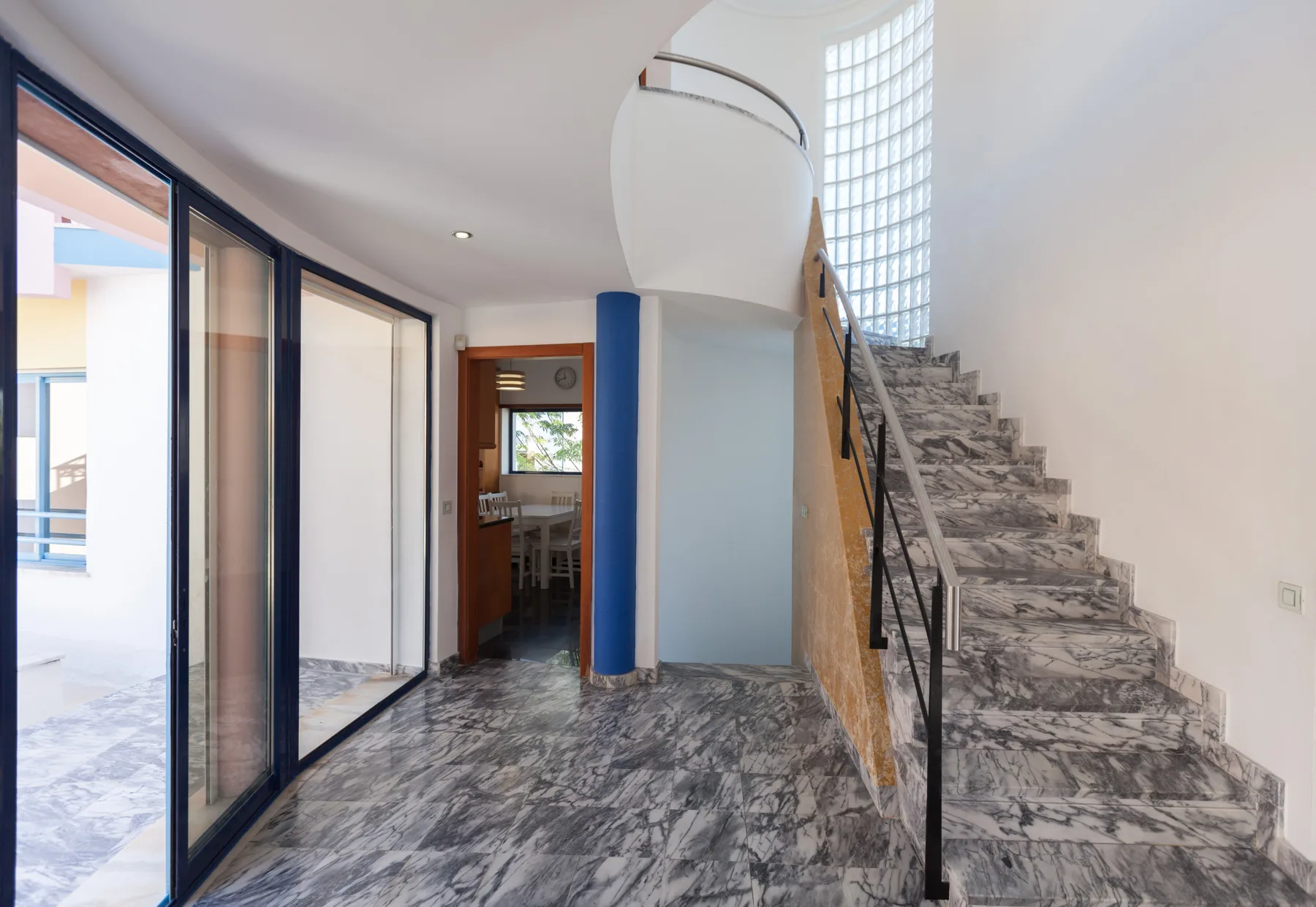 An interior entry hall with a staircase and glass doors opening to a patio.