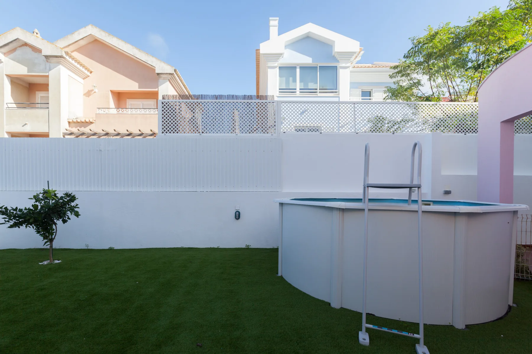 An outdoor pool stands beside a green lawn and white boundary wall.