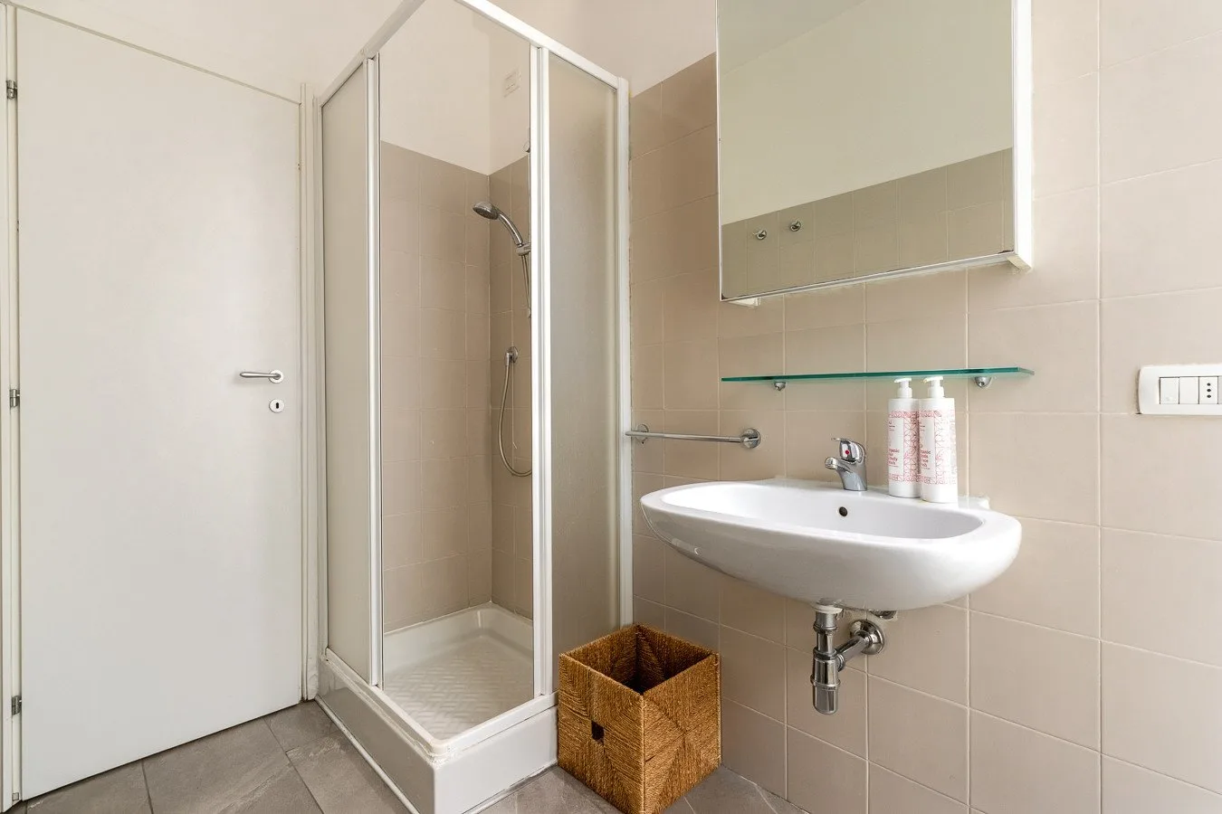 Un baño alicatado con ducha, lavabo de pared y espejo.