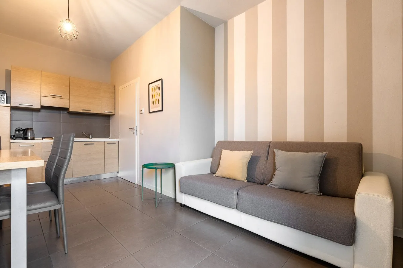 Una sala de estar con un sofá gris junto a una cocina compacta y una mesa de comedor.