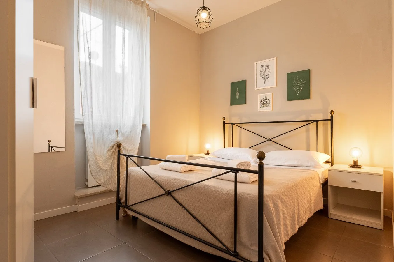 Un dormitorio con una cama de metal negro y una ventana alta con cortinas.