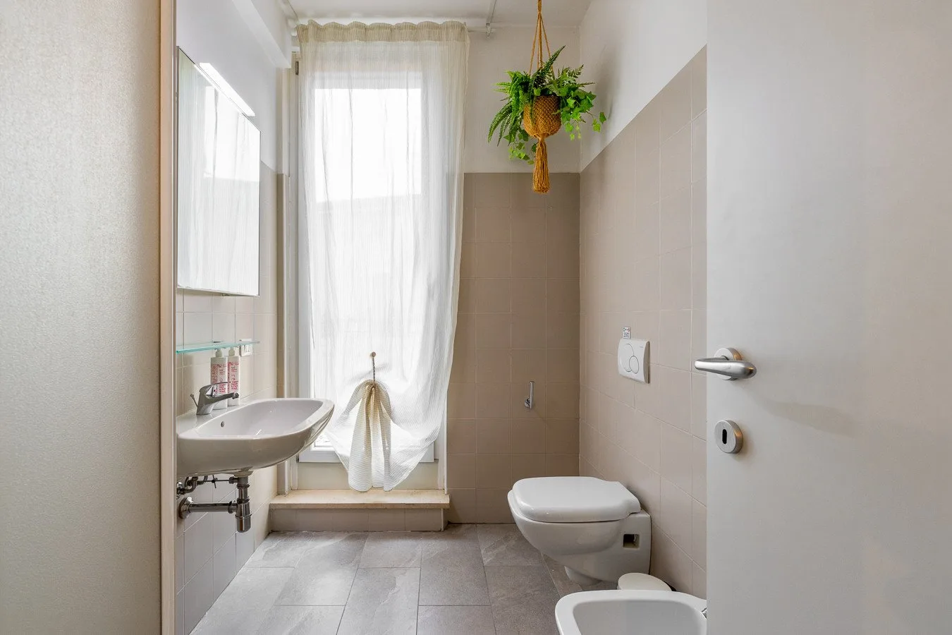Un baño luminoso tiene un lavabo, un inodoro y una zona de ducha junto a la ventana.