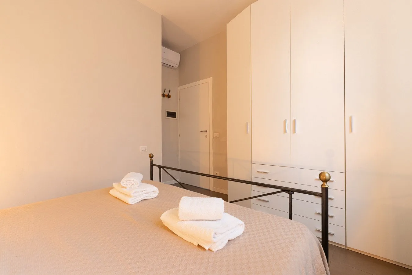 Un dormitorio con toallas blancas dobladas sobre la cama y un armario alto.