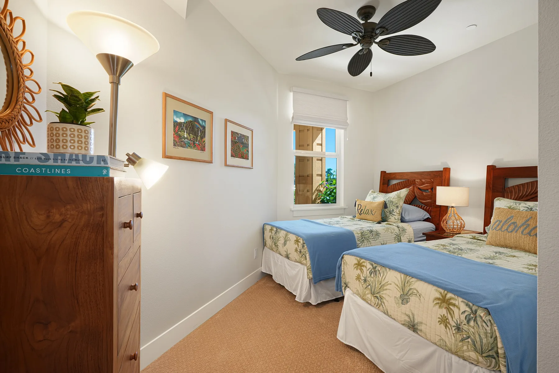 A bright bedroom with two beds, framed artwork, and a ceiling fan.