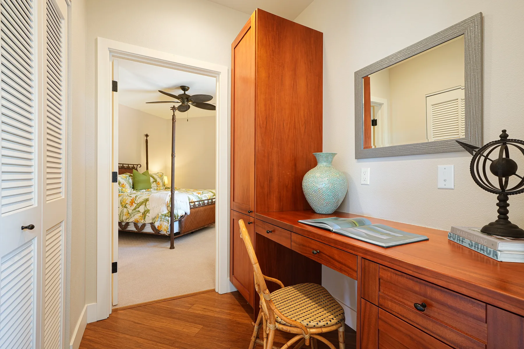 A wooden dressing table with a mirror stands beside an open doorway to a bedroom.