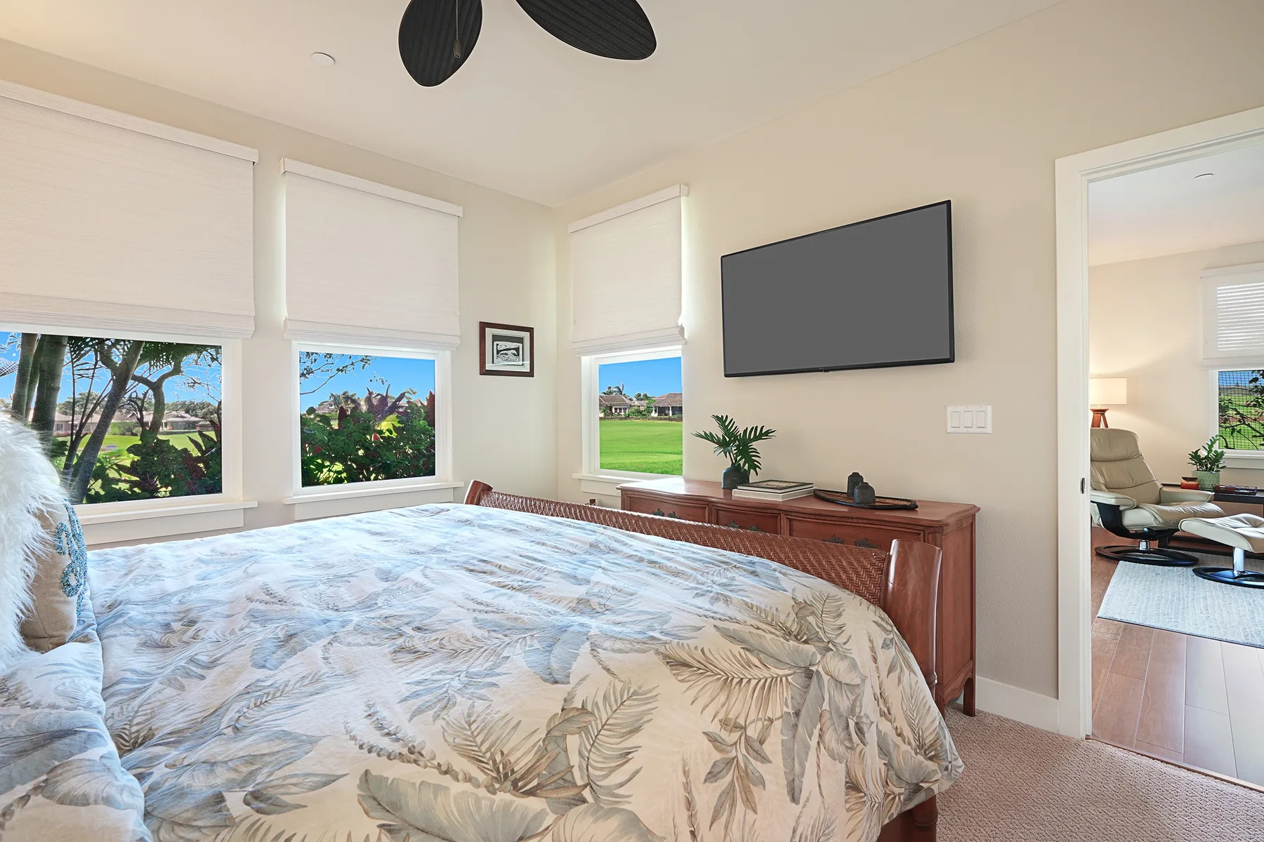A bedroom with a bed beneath a wall-mounted television and windows overlooking greenery.