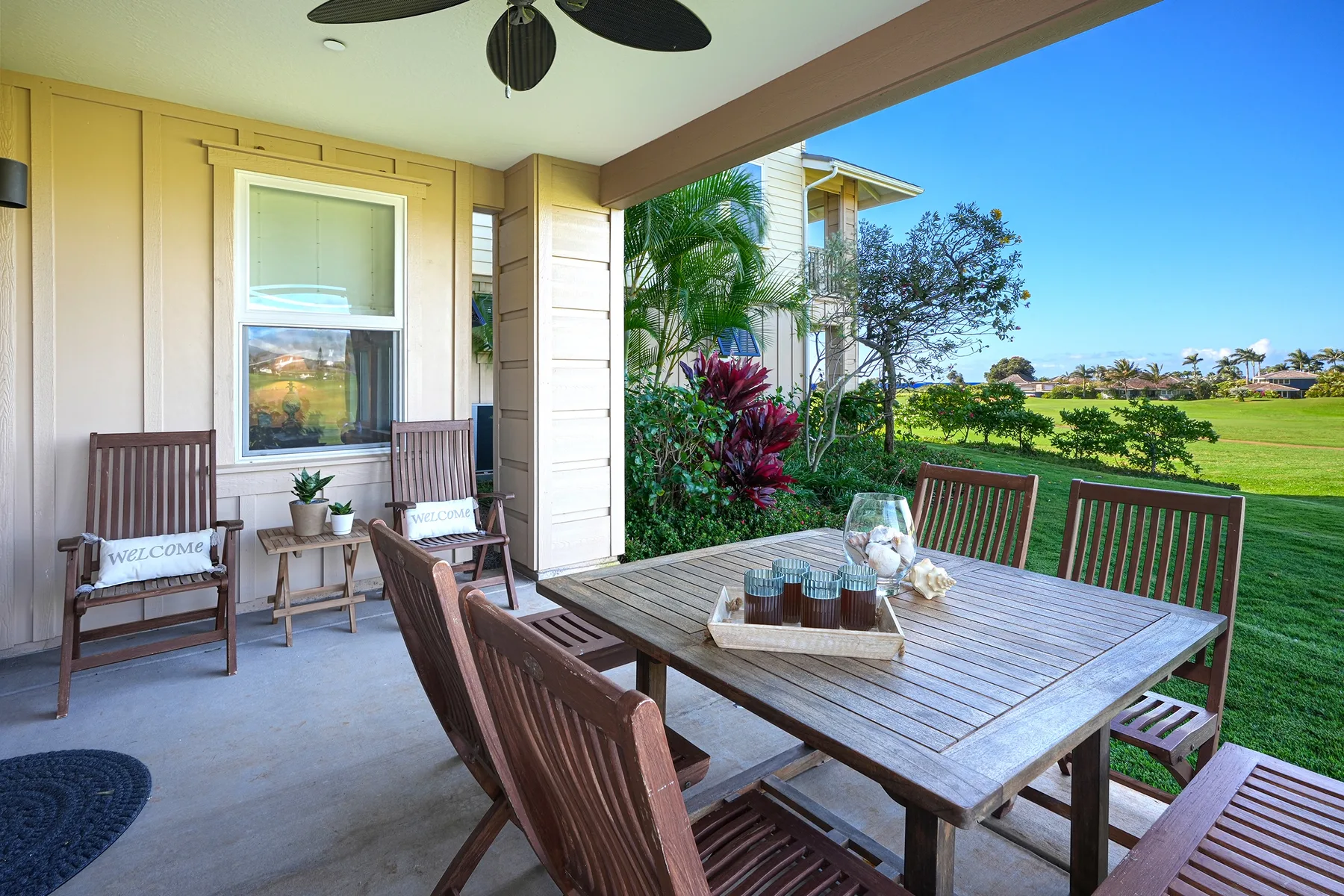 A covered patio with a wooden dining table and chairs overlooks a green lawn.