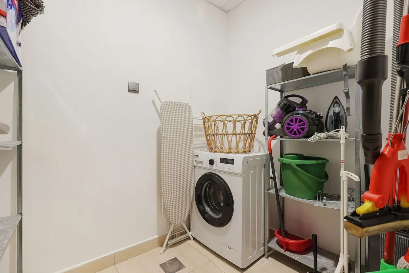 Un cuarto de lavandería con lavadora, tabla de planchar y estantes de almacenamiento.