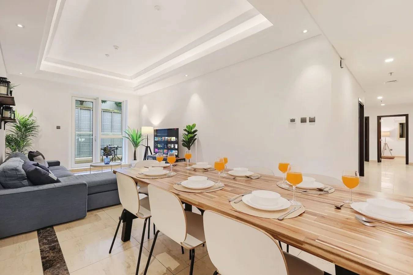 Un comedor luminoso con una mesa larga preparada junto a una sala de estar.
