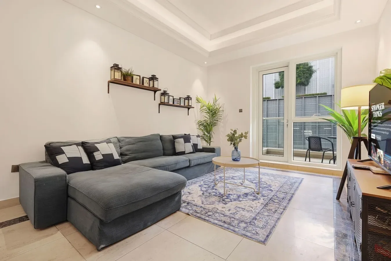 A bright living room with gray seating, a patterned rug, and large windows.