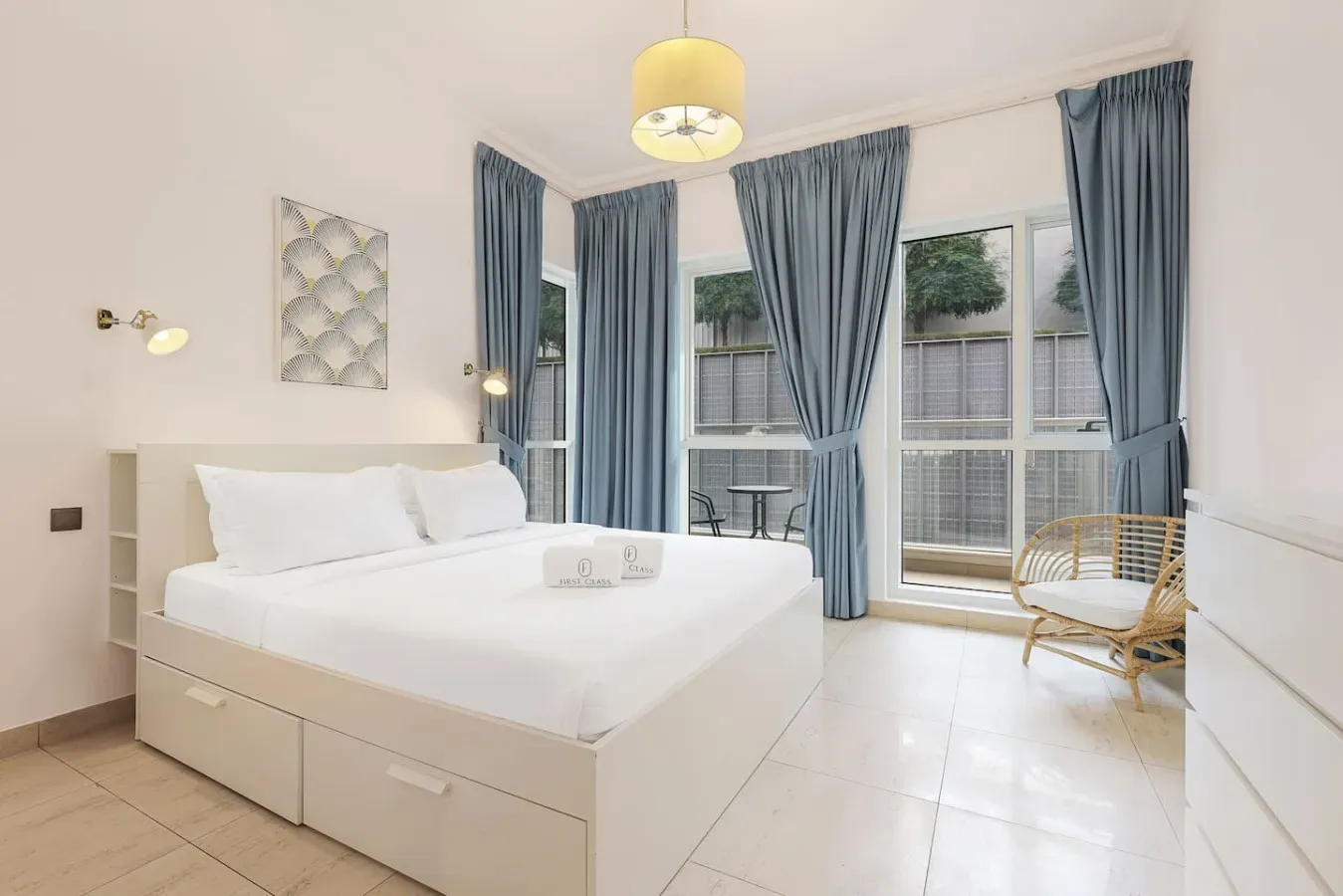 A bright bedroom with a white bed and tall windows framed by blue curtains.