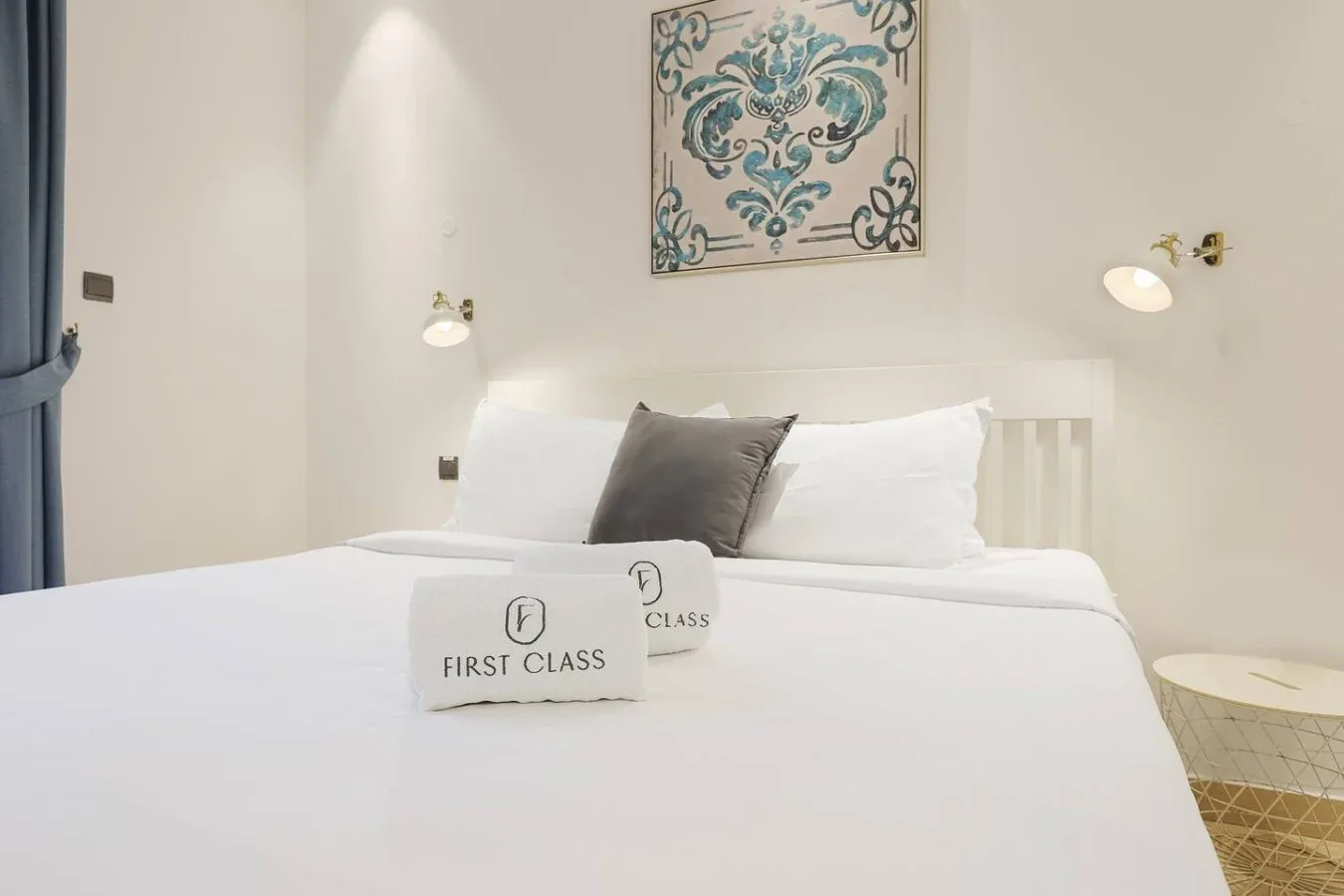 Una cama bien tendida con ropa de cama blanca y una obra decorativa sobre el cabecero.