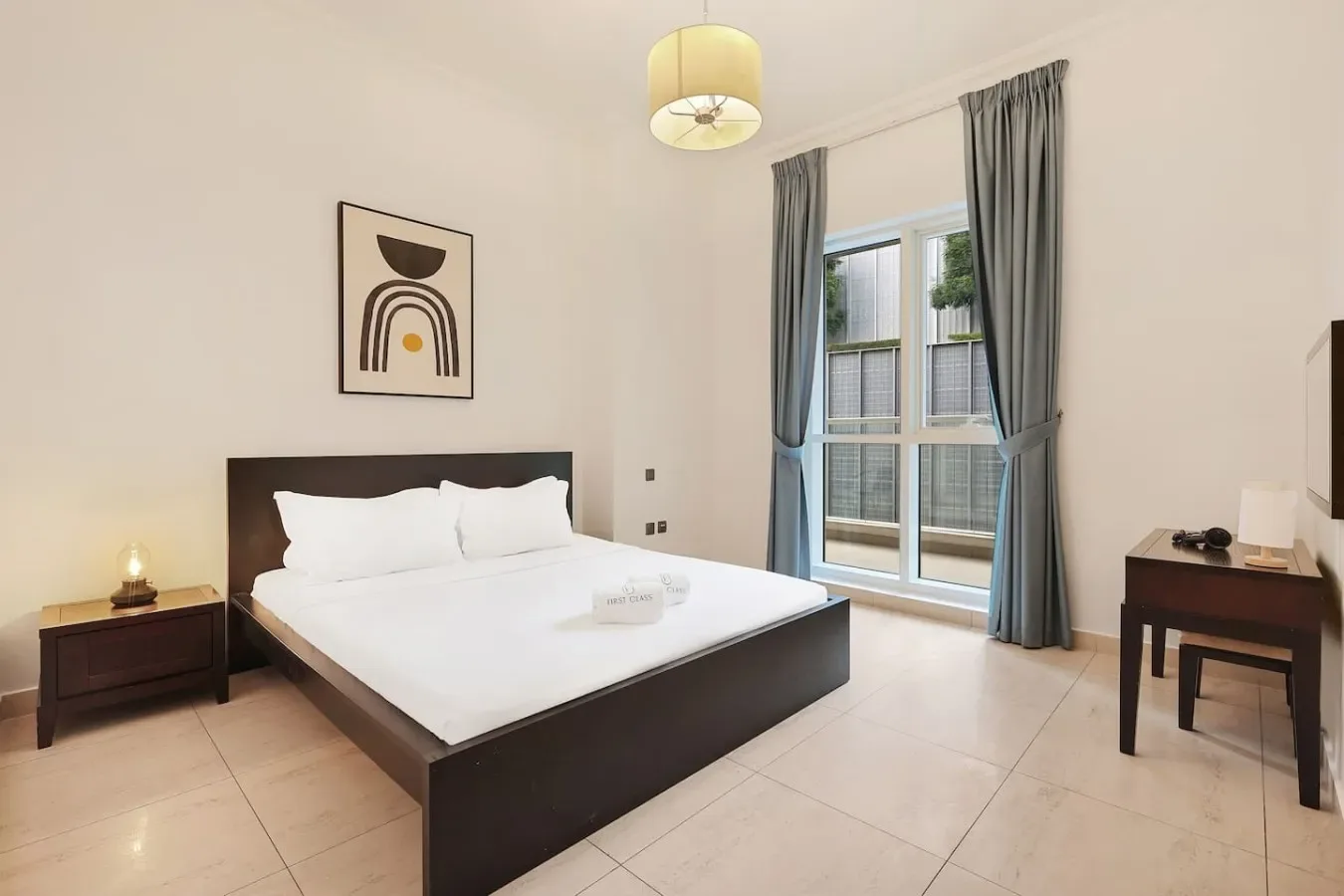Un dormitorio con una cama oscura, ropa de cama blanca y ventanas altas con cortinas.