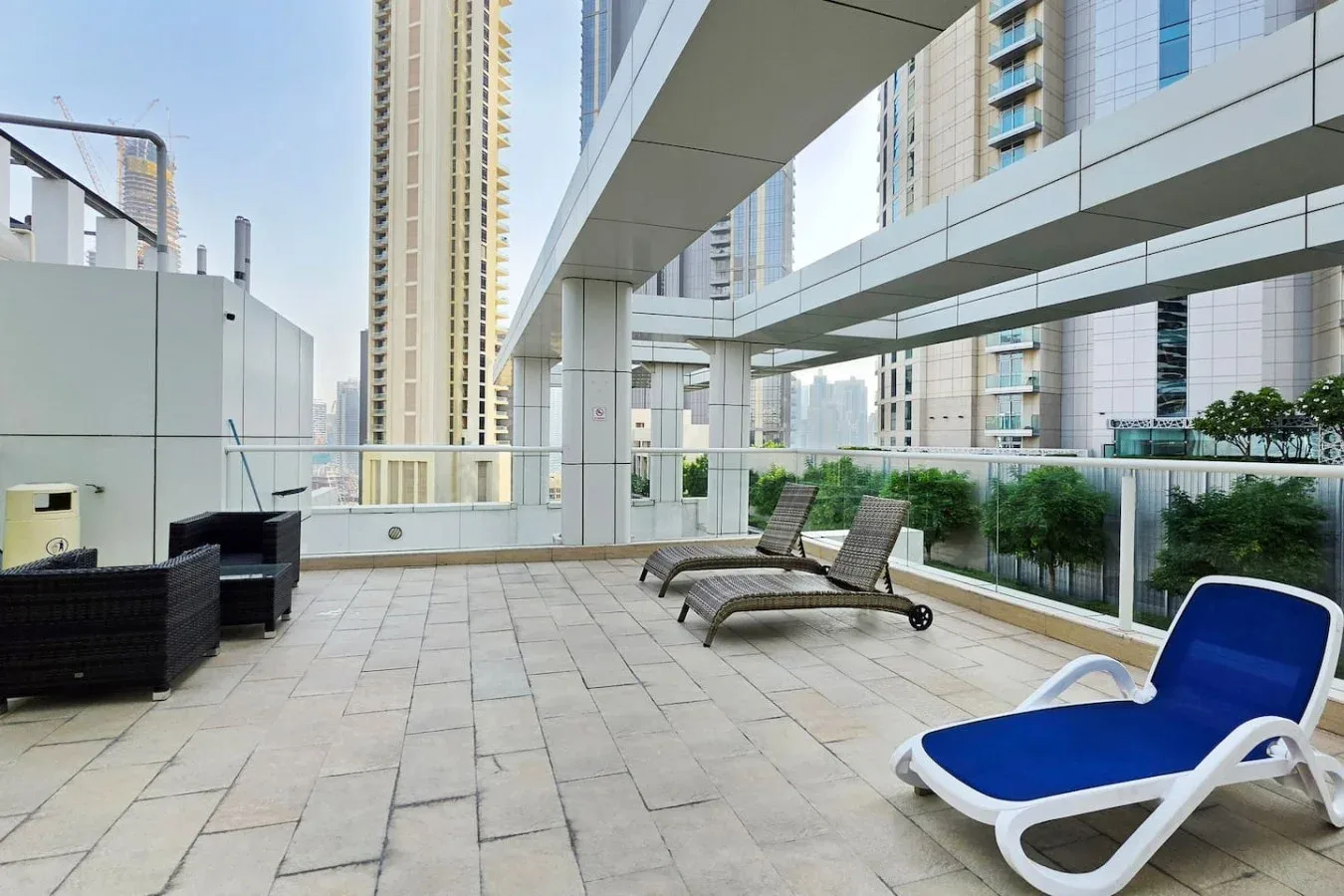 Una terraza al aire libre con asientos reclinables y barandillas de vidrio entre edificios altos.