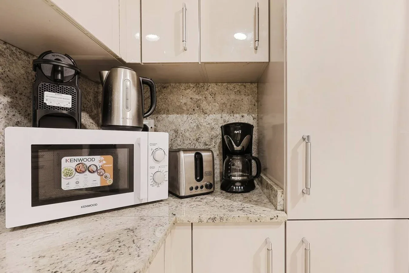 Una encimera de cocina con microondas, hervidor, tostadora y cafetera.