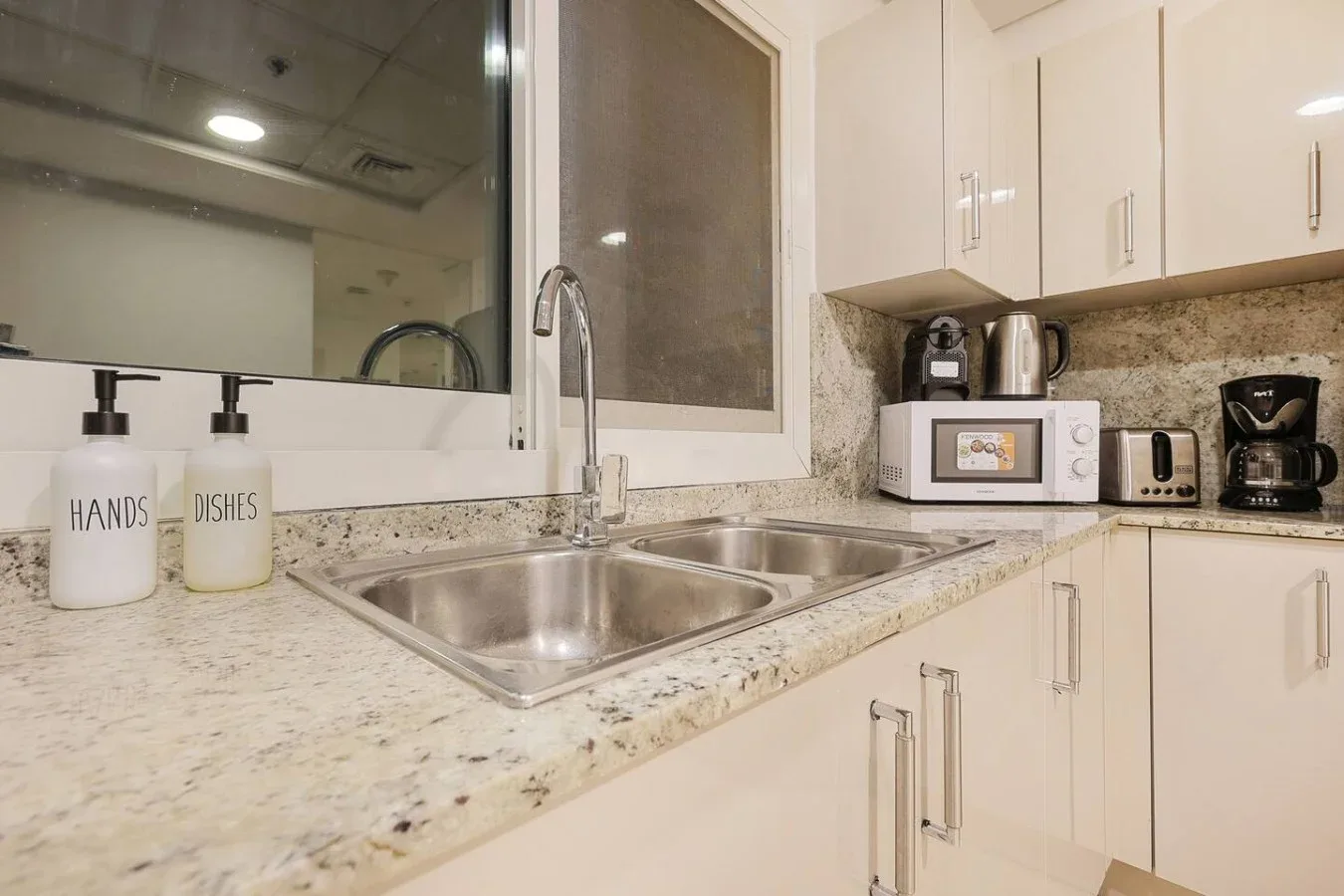 Una encimera de cocina luminosa con fregadero doble, gabinetes blancos y pequeños electrodomésticos.