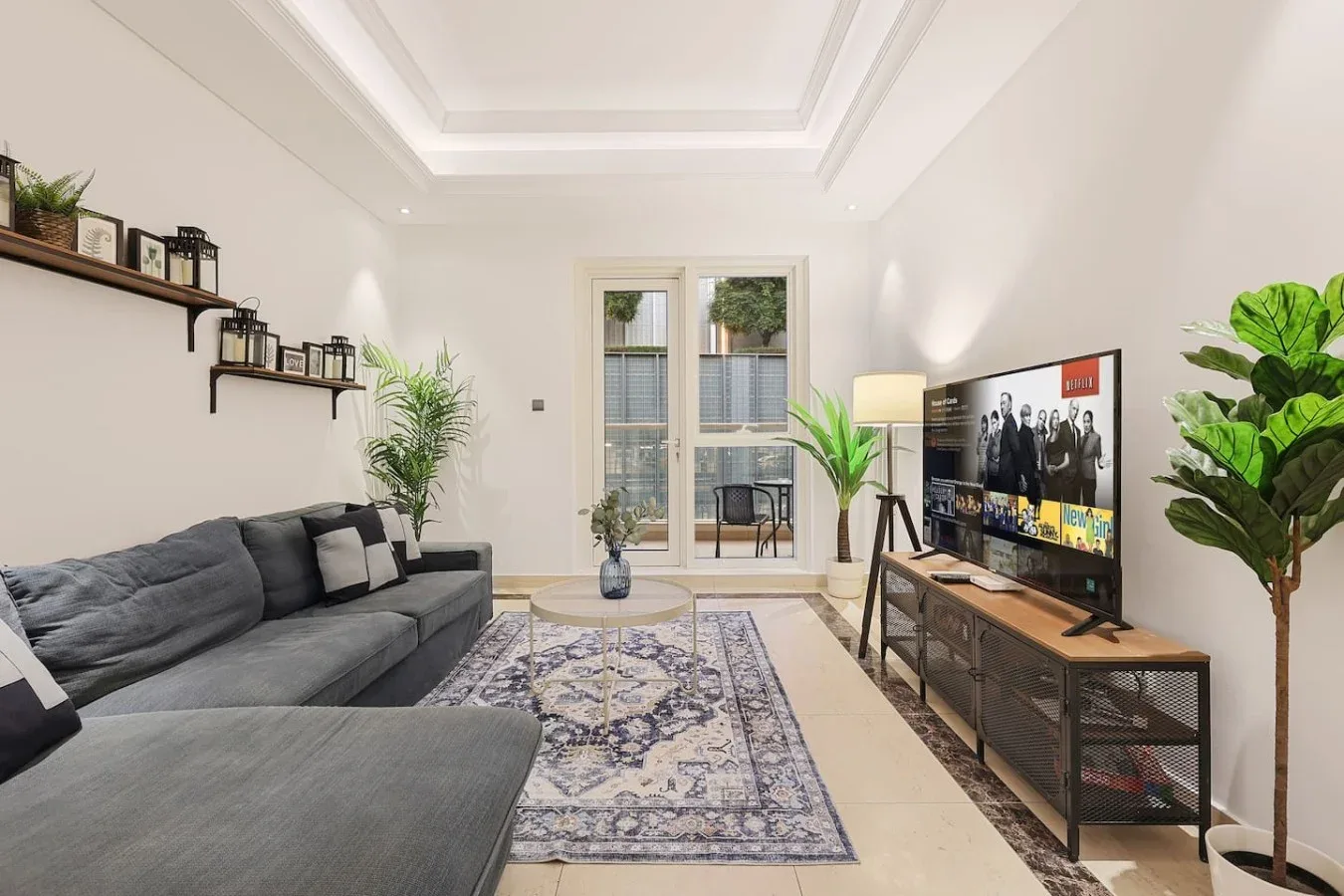 Una sala luminosa con sofá seccional gris, alfombra estampada y televisor.