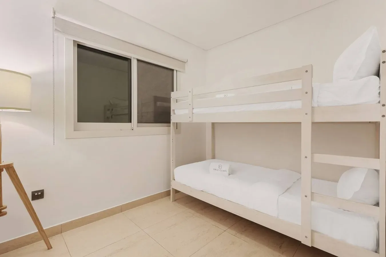 Un dormitorio luminoso con literas, ropa de cama blanca y una ventana.