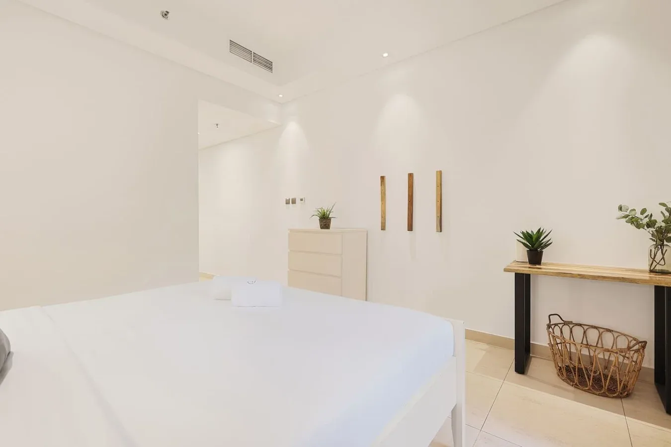 Un dormitorio luminoso con una cama blanca y una cómoda pequeña.