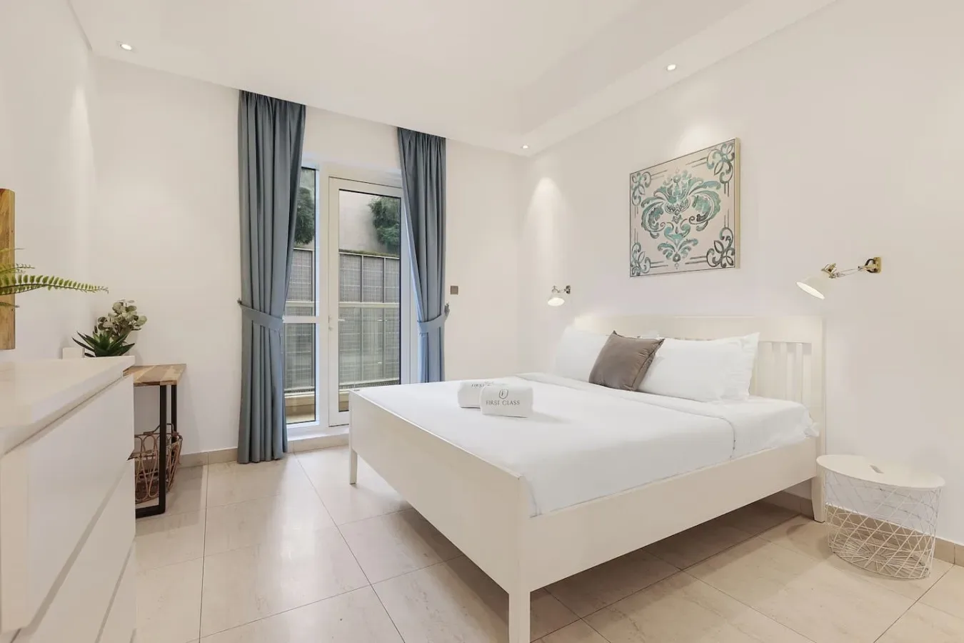 Un dormitorio luminoso con una cama blanca, cortinas azules y una puerta de cristal.