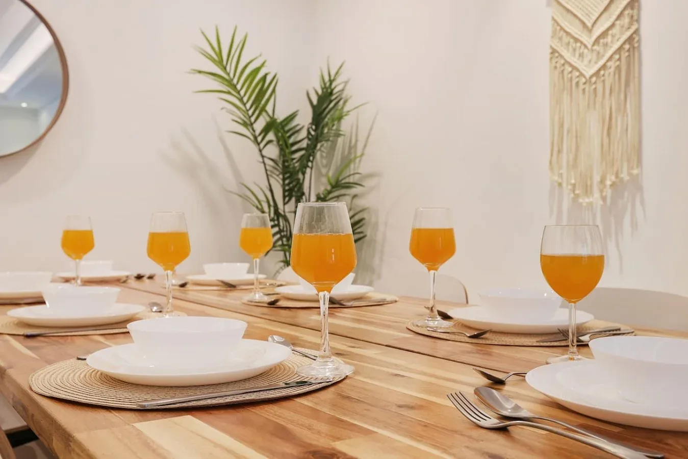 Una mesa de comedor está puesta con platos, cubiertos y vasos con bebidas de color naranja.