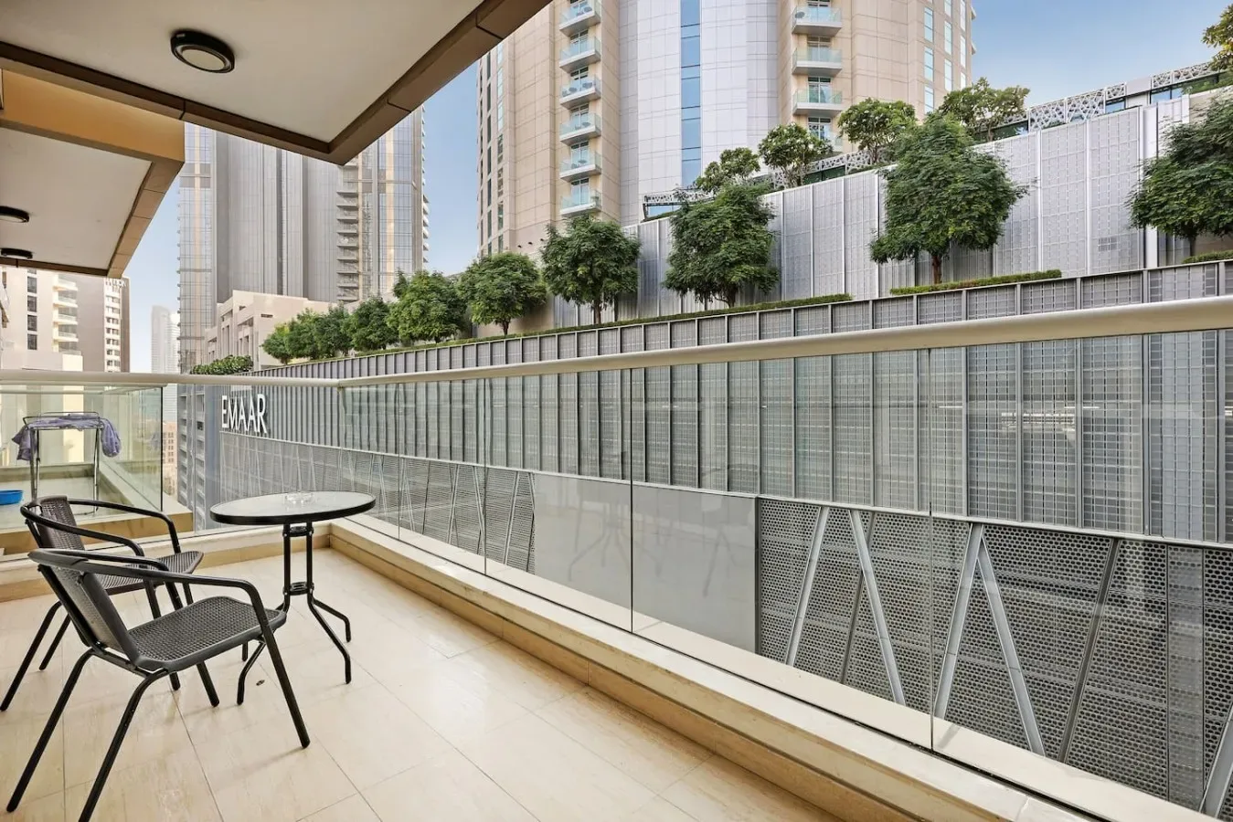 A balcony seating area overlooks a fenced urban courtyard and nearby high-rise buildings.