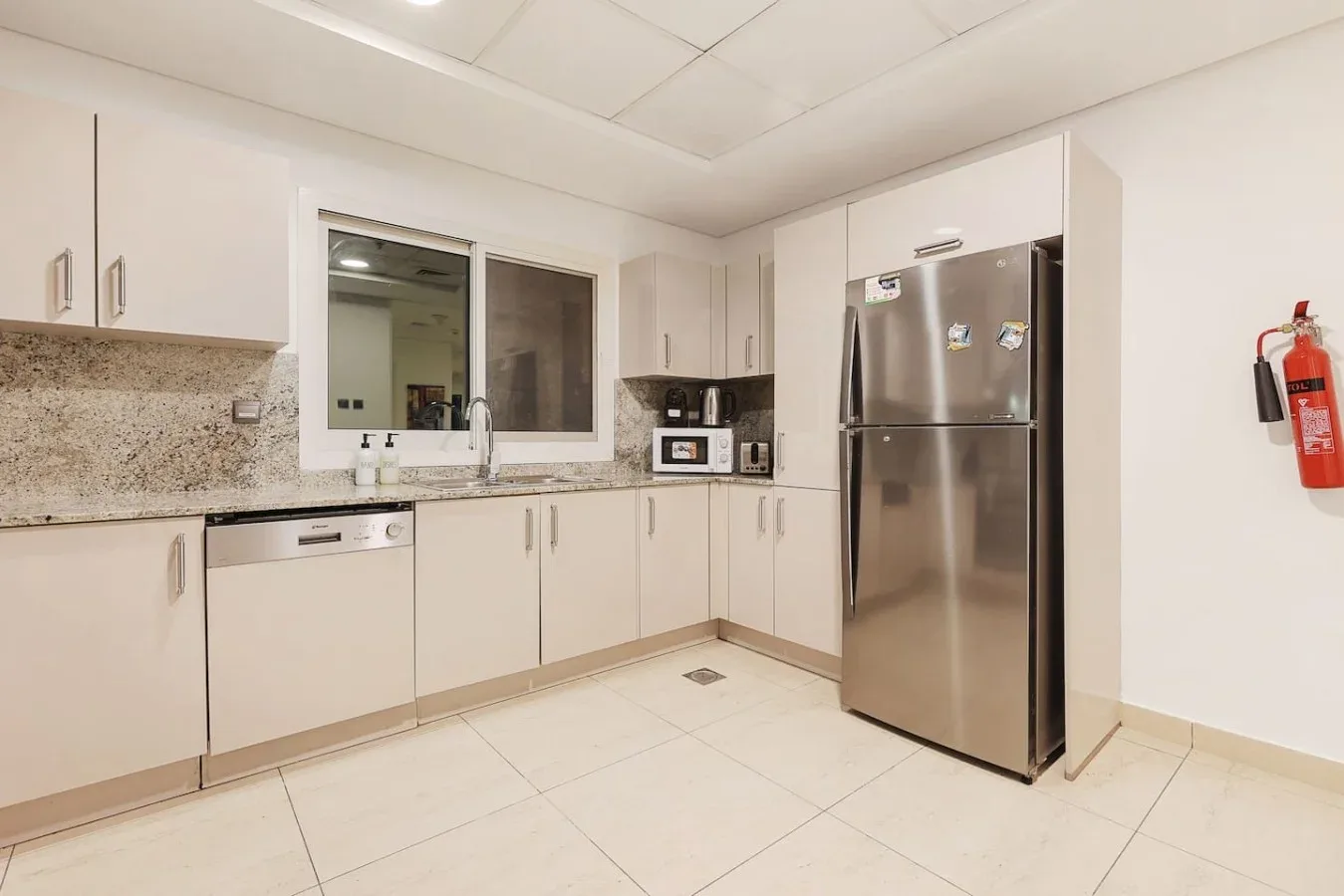Una cocina luminosa con gabinetes blancos, un refrigerador de acero inoxidable y una ventana sobre el fregadero.
