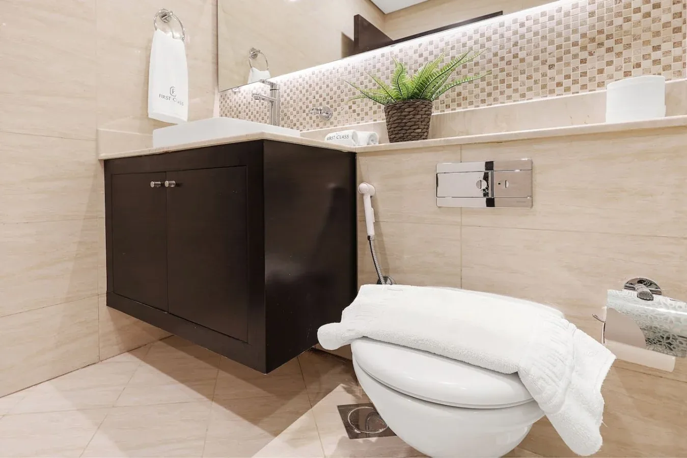 Un baño alicatado con un mueble oscuro, inodoro y toallas blancas dobladas.