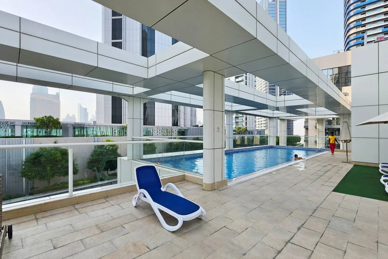 Una piscina al aire libre con una tumbona azul en la terraza pavimentada.