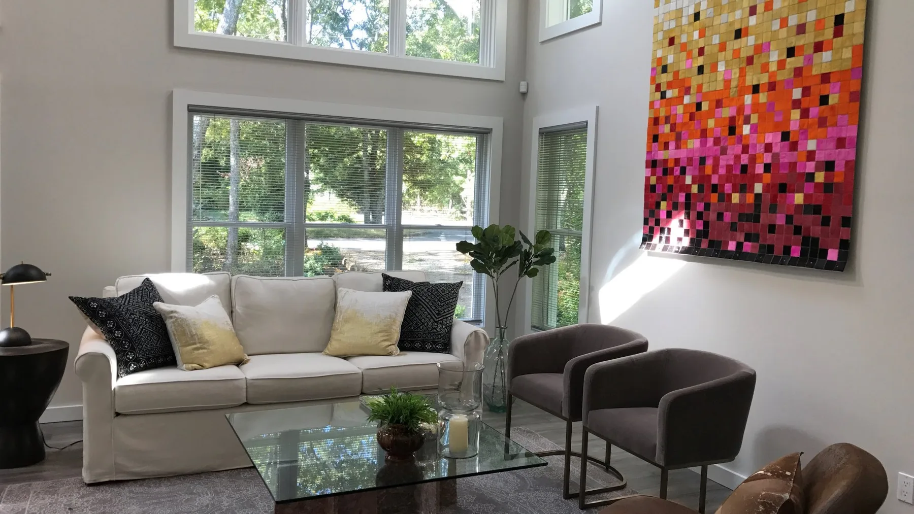 Una sala luminosa con sofá, mesa de centro de vidrio y arte colorido en la pared.