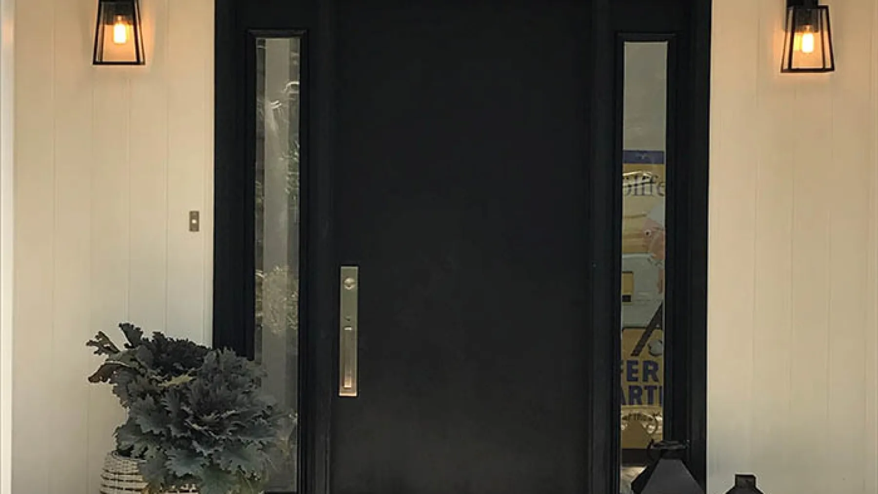 An entryway with a dark door, narrow side windows, and wall lights.