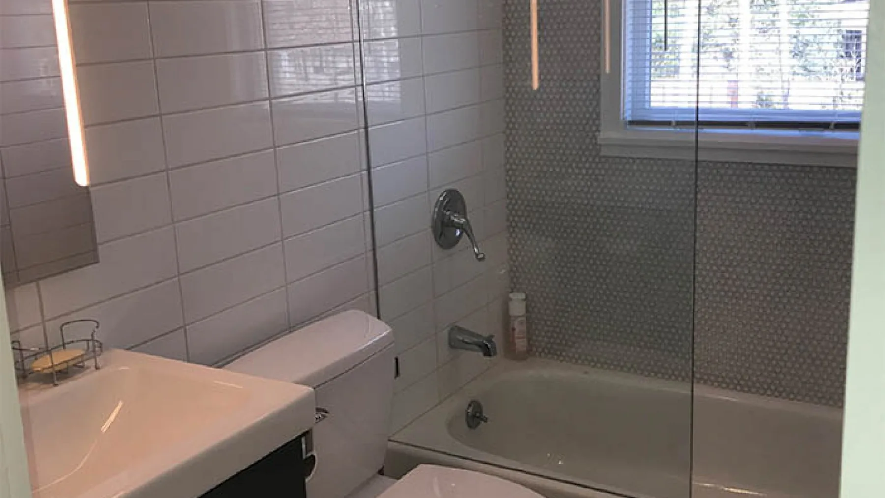 A tiled bathroom with a sink, toilet, and bathtub beneath a window.
