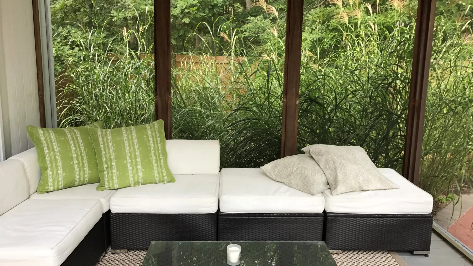 Una zona de estar luminosa con cojines blancos junto a grandes ventanas con vistas a la vegetación.