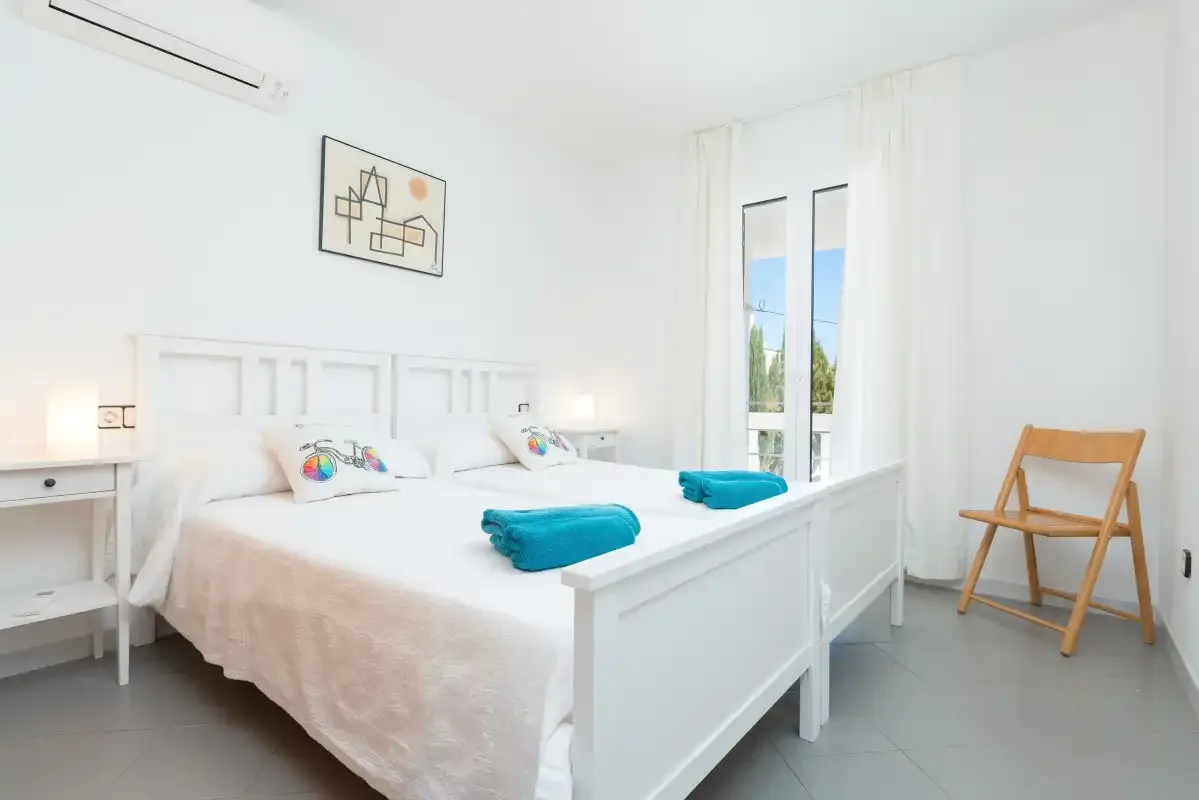 A bright bedroom with a white bed, turquoise towels, and tall windows.