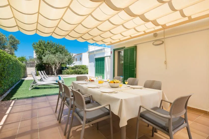 A covered outdoor dining area with a table and chairs beside a garden.