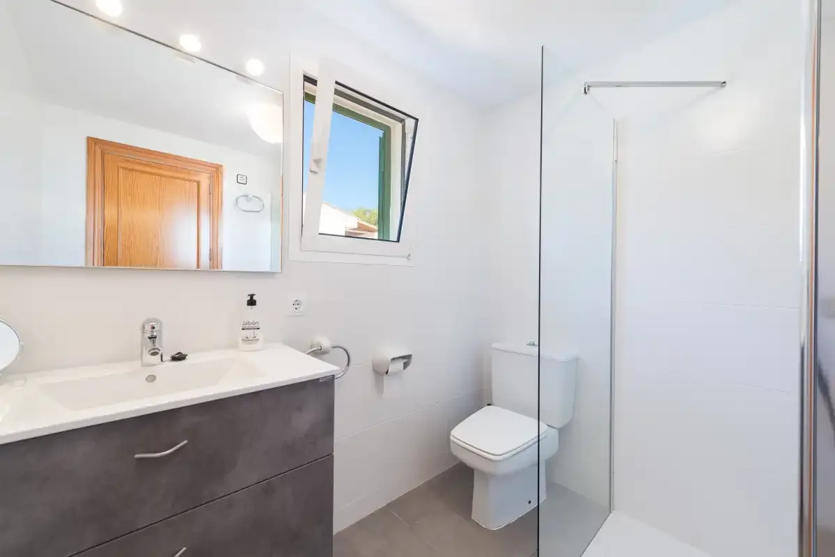 A bright bathroom with a vanity, toilet, and shower.
