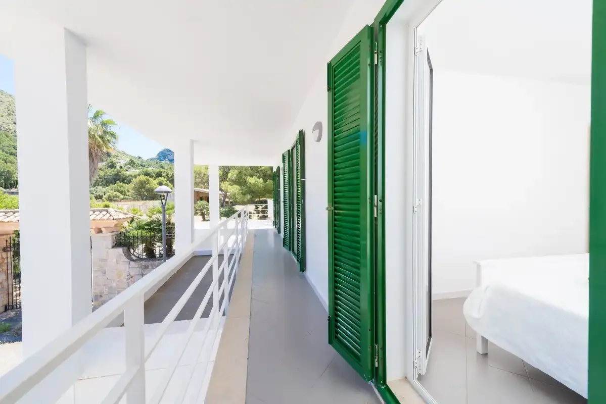 A bright covered balcony corridor with green shutters and white railings.