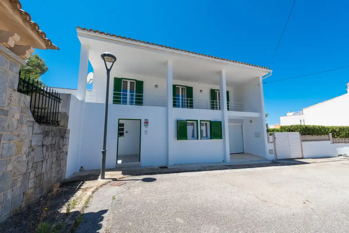 A white two-story building with green shutters stands beside a paved street.