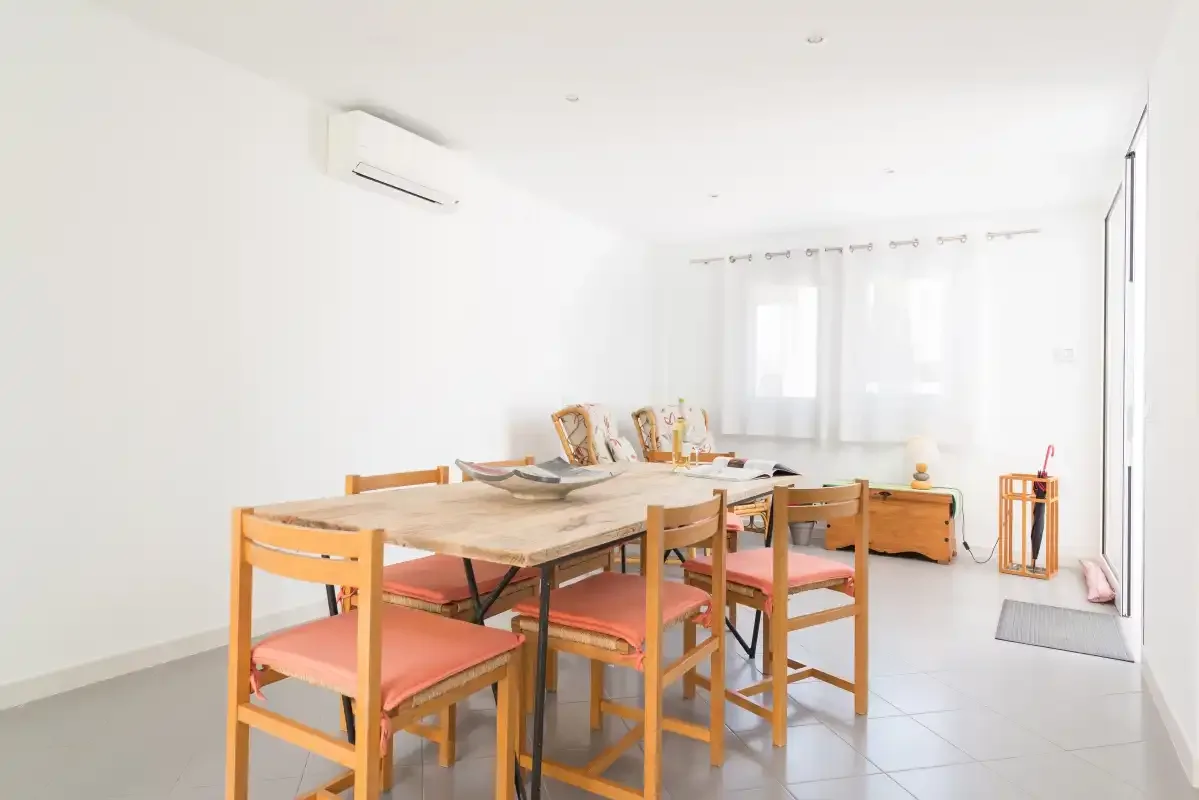 A bright dining area with a wooden table and chairs beside curtained windows.