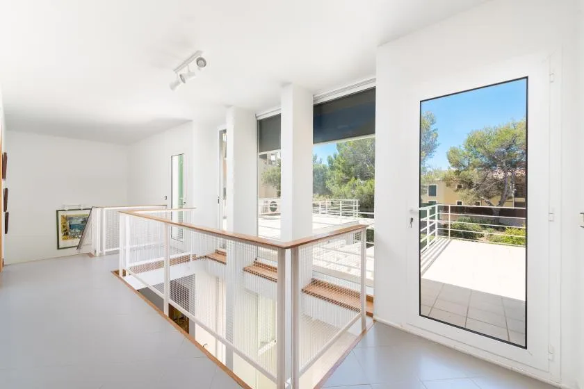 A bright interior landing opens onto a balcony with views of trees.