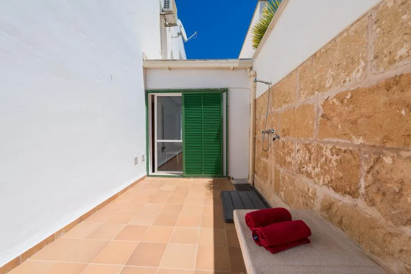 A sunlit outdoor terrace with tiled flooring, a green shutter, and seating.