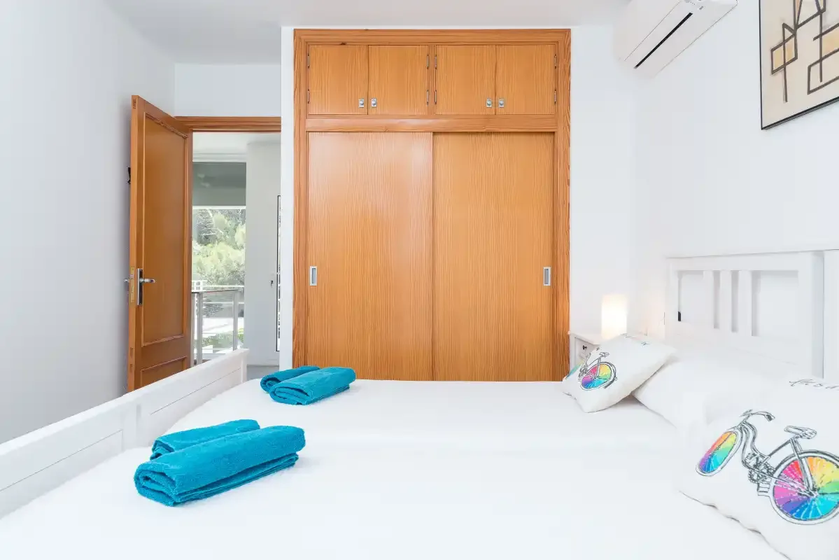 A bright bedroom with white bedding and wooden wardrobes.