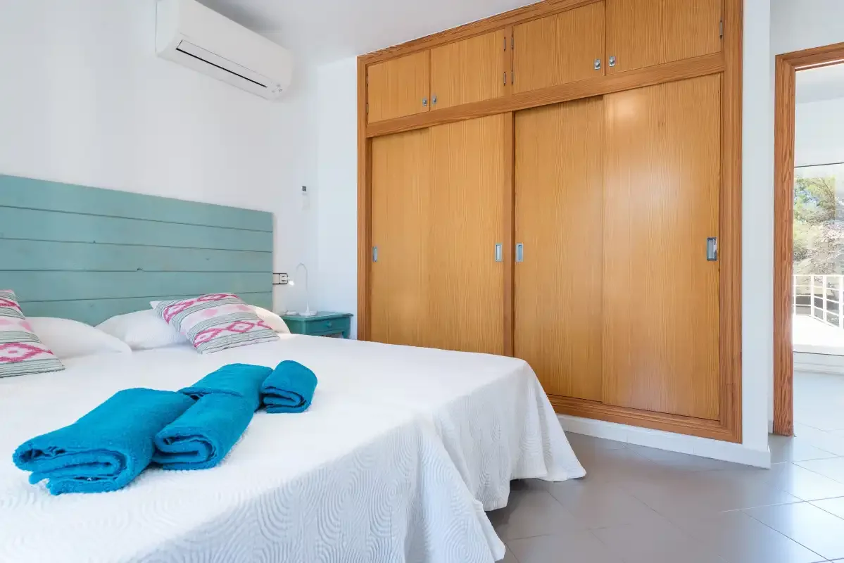 A bedroom with a bed, folded blue towels, and built-in wooden wardrobes.