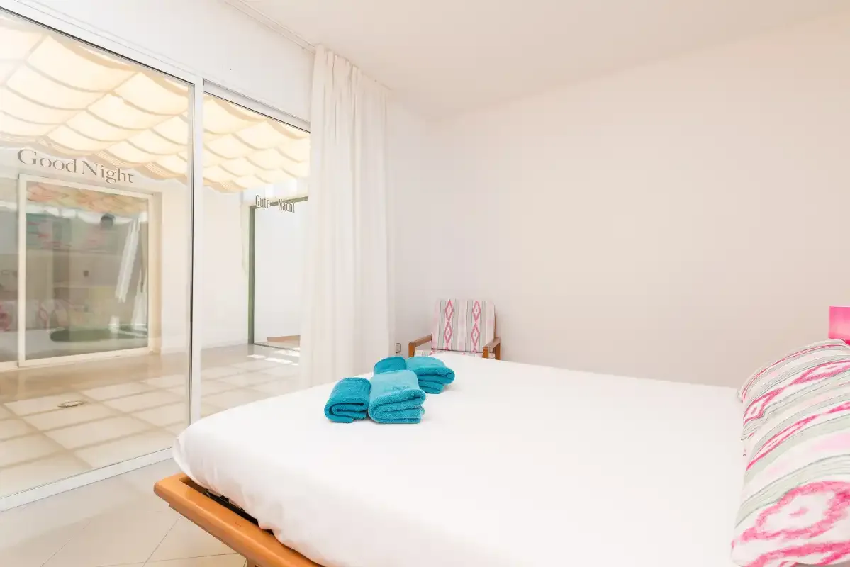 A bright bedroom with white bedding and sliding glass doors.