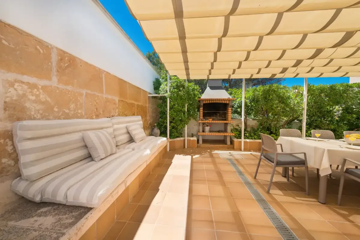 A shaded outdoor patio has cushioned seating, a dining table, and a built-in grill.