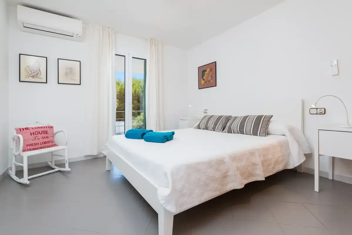 A bright bedroom with a neatly made bed and tall glass doors.